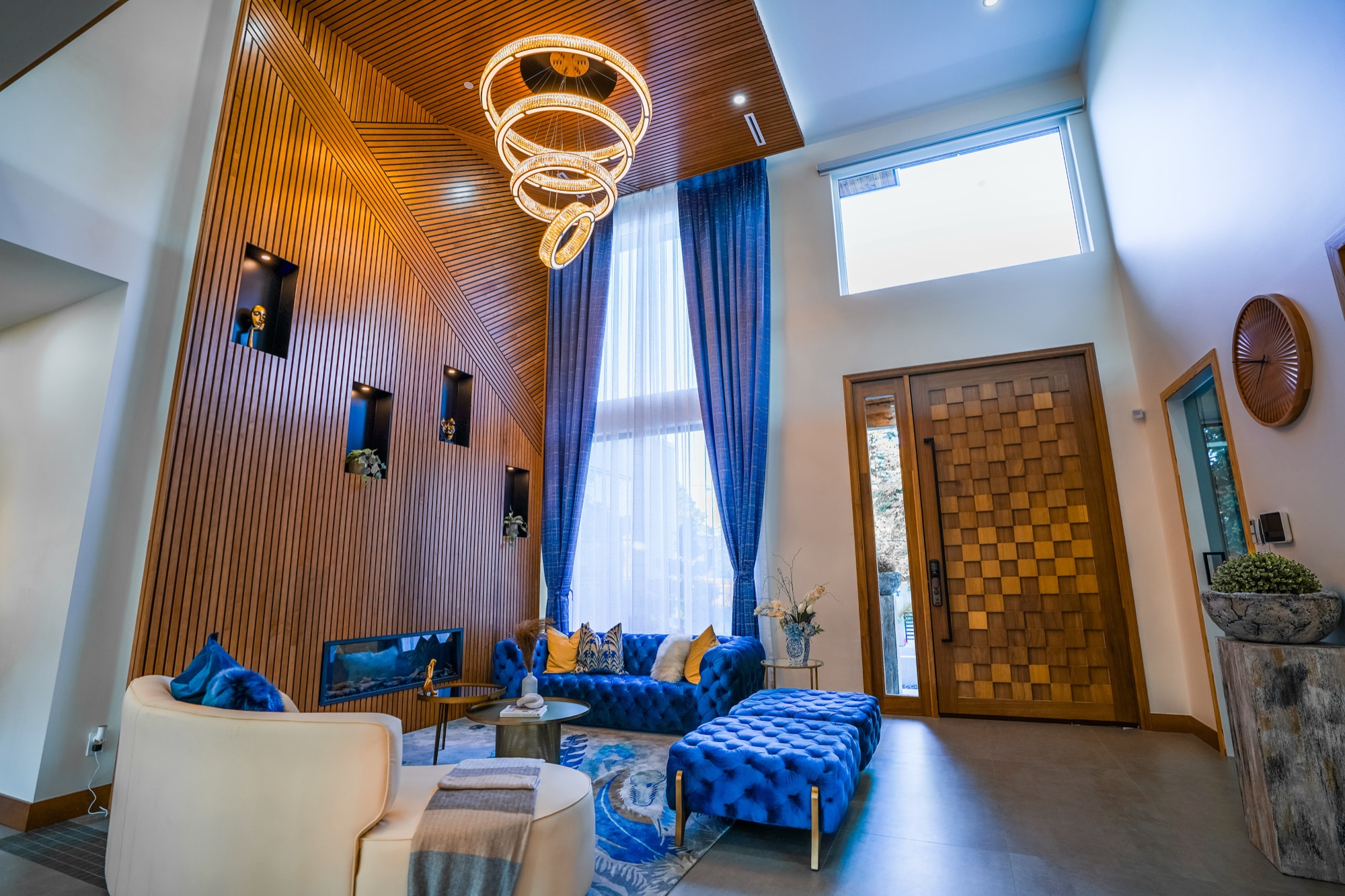 Double-height entry and living room of a completed custom home, with a tiered chandelier and slatted cedar feature wall