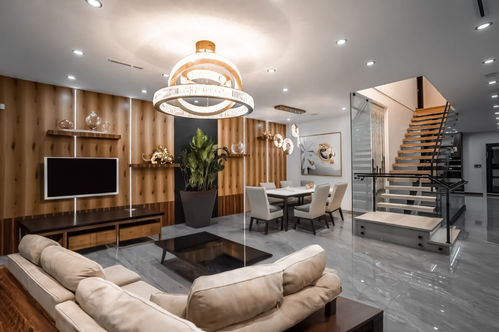 Living and dining room of a completed custom home, with a tiered chandelier, cedar feature wall and open-riser staircase
